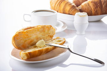Breakfast. Croissant with butter, coffee and soft-boiled egg. High key. Selective focus.
