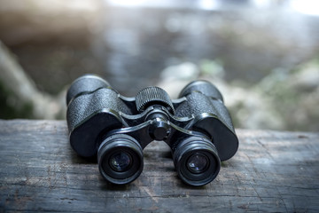 Close up old binoculars on wood with the waterfall behind.