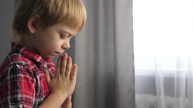 little son boy prays lifestyle bedtime religion concept. prayer child indoors praying by bed in front of window