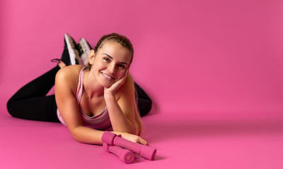Obraz na płótnie Canvas Athletic woman with dumbbells lying on pink background with copy space