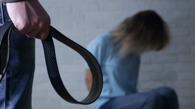 Woman trying to hide herself while man standing with belt in hand - domestic violence, abuse and people concept