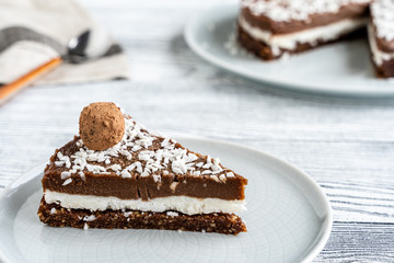 piece of chocolate cake on a plate. Chocolate and coconut cake on a white wooden background. Foodfoto in a high key. Raw dessert
