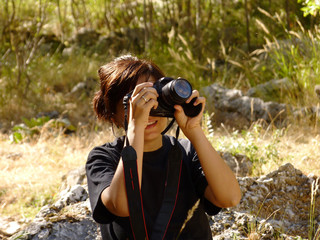 Young girl taking shots with her new digital photographing camera outdoors in the nature, sunny day