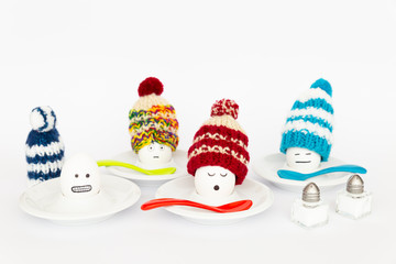 Fun breakfast concept with boiled eggs with abstract happy, sleepy, frozen and annoyed human faces wearing knitted woolen hats on white background.