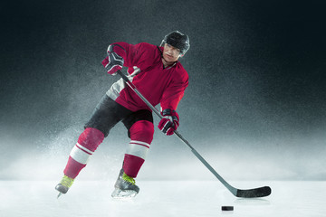 Fighting. Male hockey player with the stick on ice court and dark background. Sportsman wearing equipment and helmet practicing. Concept of sport, healthy lifestyle, motion, movement, action.