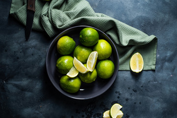 Fresh ripe limes and knife in black bowl. Sliced. Dark, metal background. Overhead view.