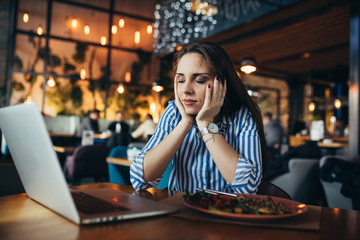 depressed and overworked woman in restaurant using laptop and having lunch