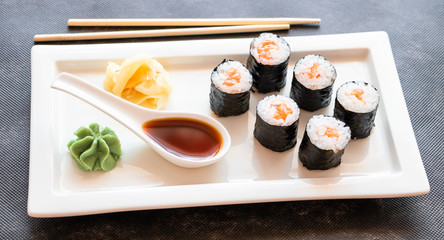 Selective focus to rolls of seaweed, rice and salmon near wasabi and soy sauce on a light  plate. Asian food.