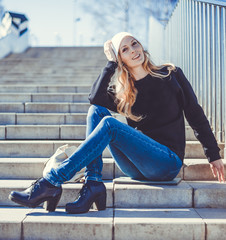 Fashion photo of a young beautiful woman in jeans, a black sweatshirt, a white knitted hat with a backpack