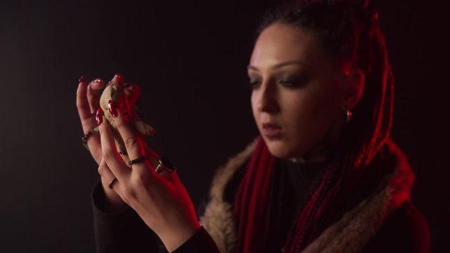 Smiling witch sticking needle in voodoo doll in smoke