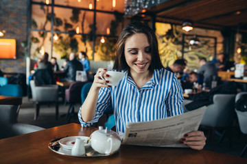 young woman enjoying tea and reading press in cafe bar
