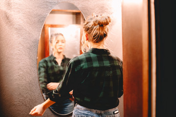 Young confident woman looking at herself in the mirror while standing in hallway at home getting...