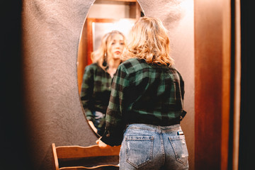 Young woman looking at herself in the mirror while standing in hallway at home getting ready before...