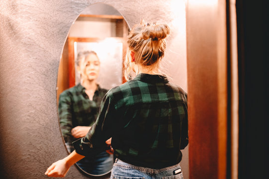 Young confident woman looking at herself in the mirror while standing in hallway at home getting ready before going out