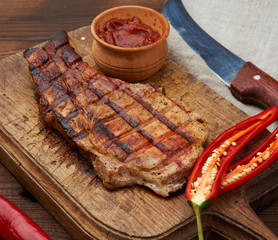 pork fried steak on the rib lies on a vintage brown wooden board, next to fresh red chili peppers