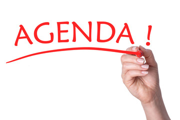 Hand writes word agenda with red marker.