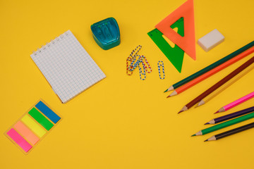 A set of stationery. Colored pencils, sharpener, eraser, ruler, notepad, paper clips and stickers on a yellow background, space for text. Flat lay. school supplies. office