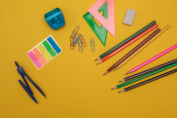 A set of stationery. Colored pencils, sharpener, eraser, ruler, notebook, paper clips, pair of compasses and stickers on a yellow background, space for text. school supplies. office