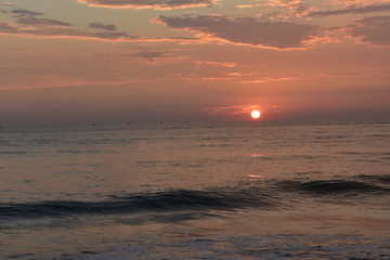 sun setting in a ocean with small waves and beautiful sky