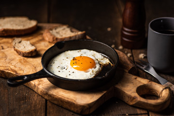 Fried egg, bread slice and black coffee.Chopping board. Dark, wooden, rustick table.