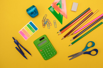 Stationery set. calculator, colored pencils, sharpener, eraser, ruler, scissors, paper clips and stickers on a yellow background, space for text. Flat lay. school supplies. office