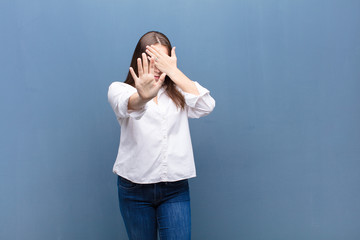 young blonde pretty girl covering face with hand and putting other hand up front to stop camera,...
