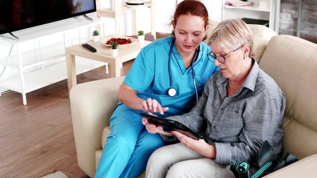 Female nuse helping senior elderly retired woman how to use her tablet computer