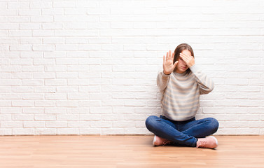 young blonde pretty girl covering face with hand and putting other hand up front to stop camera,...