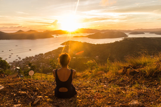 backview of girl, sitting on the earth and observing sunset in Coron city view point with sea and sky on the background