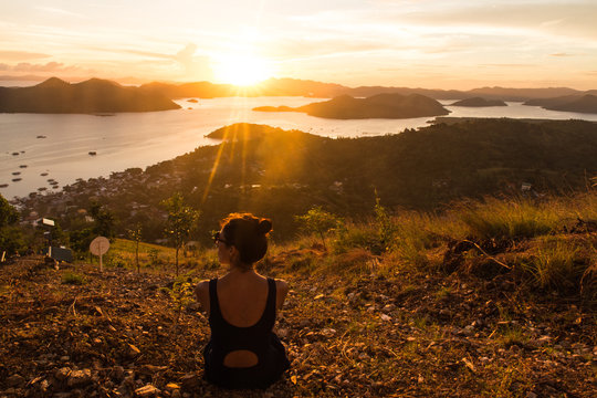 backview of girl, sitting on the earth and observing sunset in Coron city view point with sea and sky on the background
