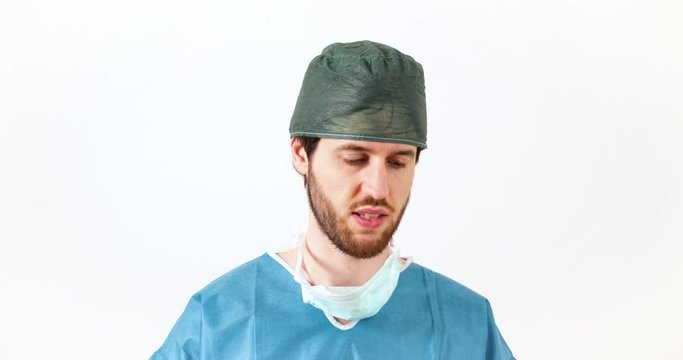 Giovane ragazzo medico con barba lunga e mascherina abbassata legge su un foglio e parla per al conferenza stampa di fronte la telecamera. Sfondo bianco.