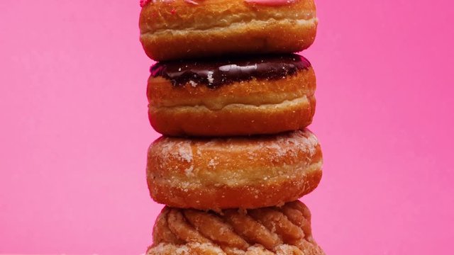 Donuts pile in the middle of the frame spinning around. Stop motion animation with a bright pink background. Pop art concept.