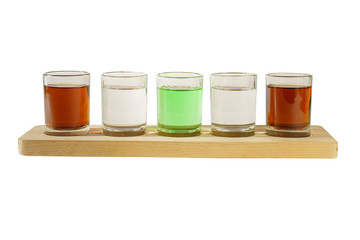 Multicolored transparent cocktails, a set of shots in one row, five servings on a wooden stand, substrate. Side view Isolated white background. Drink for the menu restaurant, bar, cafe