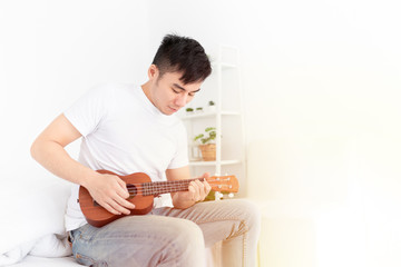 asian man artist holding and playing ukulele in his bedroom, he training to show acoustic concert, happiness activity