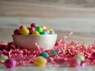 White candy bowl of jelly beans for Easter on a bed of pink paper shreds with a wooden background.