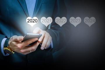 Man holding smartphone in hand display luminous 2020 number calendar year, connecting line virtual holographic glowing in background. global technology concept.