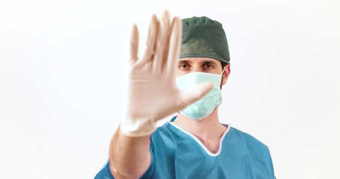 Dottore con mascherina alza la mano in segno di alt, sfondo bianco.