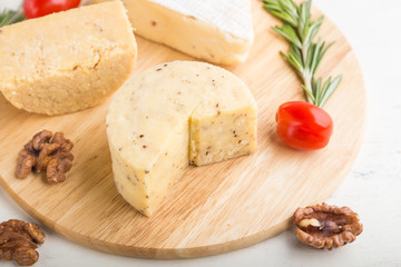 Cheddar and various types of cheese with rosemary and tomatoes on wooden board on a white background . Side view, selective focus.