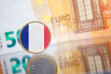 Macro photo of a coin in 1 euro with the France flag on a blurred background banknote in 50 euro. Reflection of the coin on the glass table. Very small depth of field.