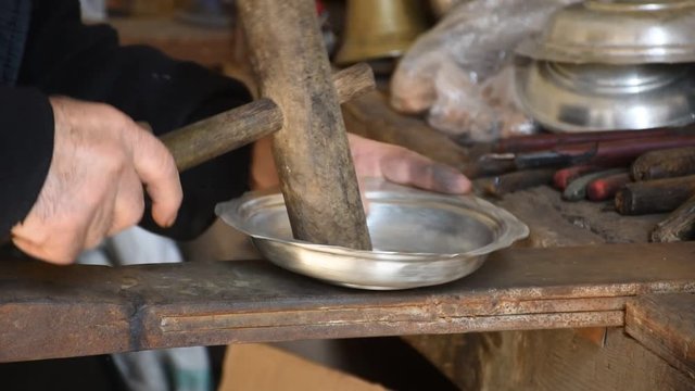 a copper plate corrected by the hands of a copper worker. straightens the plate by hitting the center with a wooden mallet.