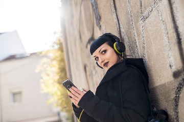 Beautiful gothic girl listening her music by headphones and walking around the city