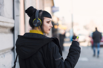 Beautiful gothic girl listening her music by headphones and walking around the city