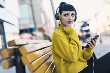 Beautiful gothic girl listening her music by headphones and walking around the city