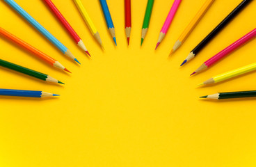 Top view of colored pencils arranged in a semicircle in the form of rays on a yellow background  