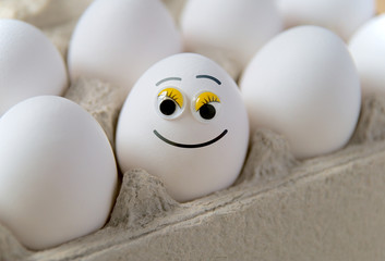Eggs in a cardboard box, one egg with a funny painted smiling face