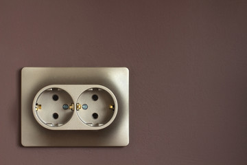 Golden double power socket on a painted brown wall. Standard european electrical connector close-up