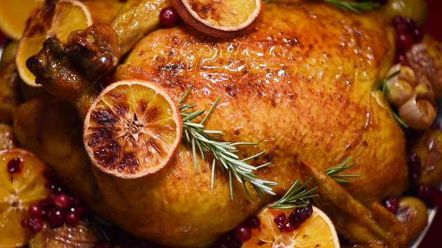 Christmas family dinner. Roasted chicken with herbs, oranges, cranberries on rotating background, slow-motion shooting.