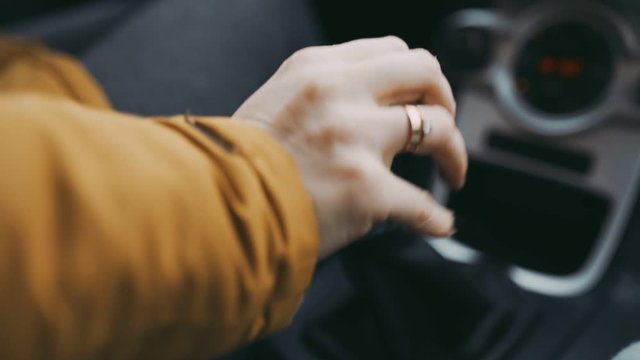 The hand of modern girl with engagement ring on her finger, slow motion. Married girl hand controls manual gearbox, shifts gears in car. Close-up of woman's hand in jacket sitting in car.