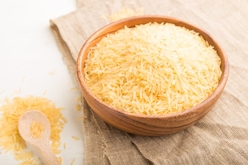 Wooden bowl with raw golden rice and wooden spoon on a white wooden background. Side view, selective focus.