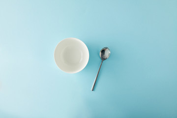 Top view of empty bowl and teaspoon on blue background